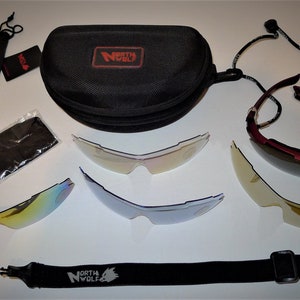 Peut inclure: Un ensemble de lunettes de soleil de sport noires avec plusieurs verres interchangeables. L'ensemble comprend un étui noir, un sac à cordon, un chiffon de nettoyage et une sangle de cou. La marque "NORTH WOLF" est visible.