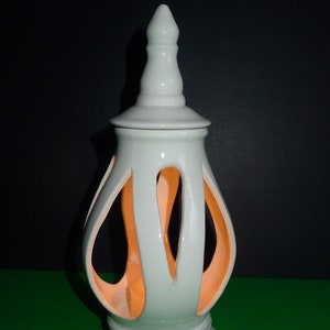 May include: White ceramic candle holder with a decorative openwork design. The holder has a round base and a pointed top.