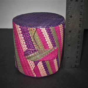 Peut inclure: Un panier tissé cylindrique avec un dessus violet et un motif rayé coloré en rose, vert et blanc.