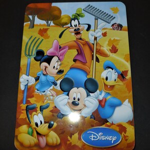 May include: A colourful illustration of Mickey Mouse, Minnie Mouse, Goofy, Donald Duck, and Pluto in an autumn setting. The characters are surrounded by orange, yellow, and red leaves. The image includes the word "Disney" in a blue oval.
