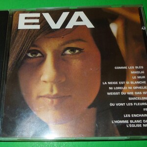 Peut inclure: Une pochette d'album de disque vinyle vintage avec le portrait rapproché d'une femme aux cheveux foncés. Le titre de l'album "EVA" est imprimé en gros caractères gras en haut de la pochette. Le dos de l'album liste les titres des chansons : "Comme Les Bles", "Mikelai", "Le Mur", "La Neige Est Si Blanche", "Ni Lorelei Ni Ophelia", "Weisst Du Wie Das Ist", "Barcelona", "Ou Vont Les Fleurs?", "Frei", "Les Enchaines", "L'Homme Blanc Dans L'Eglise Noire".