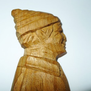 May include: A wooden carving of a person wearing a hat. The carving is detailed and shows the person's face and clothing.