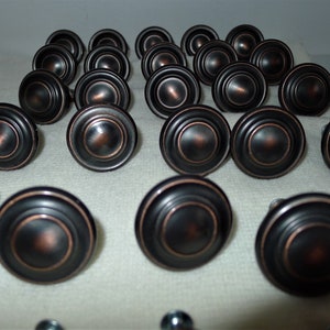 Peut inclure: Une collection de 20 boutons de porte ronds, noirs et bronze, avec un motif de cercles concentriques en relief.