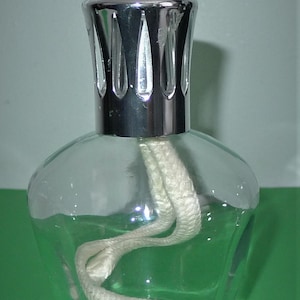 May include: A clear glass oil diffuser with a silver metal top and a white wick. The diffuser is empty and the wick is coiled inside.