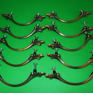 May include: Ten antique-style cabinet knobs with a decorative floral design. The knobs are made of metal and have a bronze finish. Each knob has a single screw hole for installation.