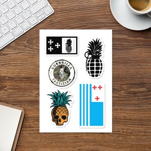 May include: A sheet of stickers featuring a pineapple design with a skull, a pineapple with a grenade, a camouflage circle with the text "Guerrilla Tactician", and a flag with a blue background and red crosses.