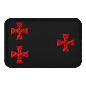 May include: Black embroidered patch with three red crosses. The crosses are in a vertical line on the left side of the patch and one cross is on the right side of the patch.