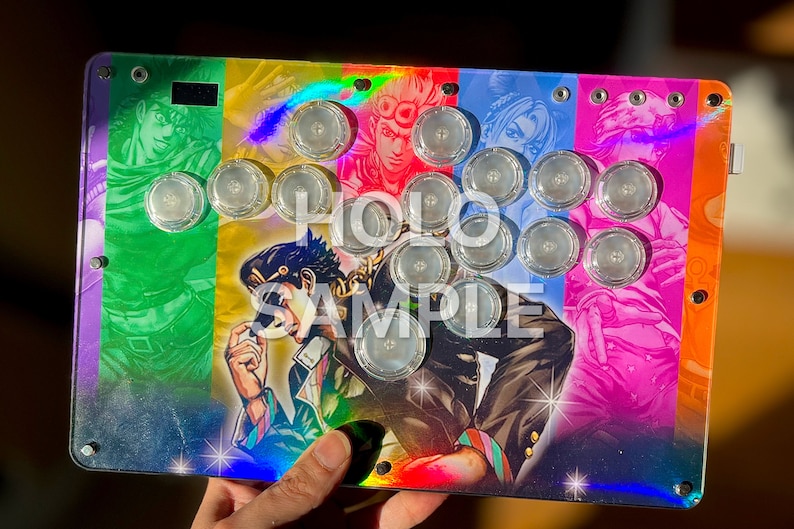 Peut inclure: Un stick arcade personnalis&eacute; avec un design color&eacute; repr&eacute;sentant des personnages d'anime. Les boutons transparents sont dispos&eacute;s selon une disposition standard. L'&oelig;uvre d'art a un effet holographique, et le texte "HOLO SAMPLE" est visible.