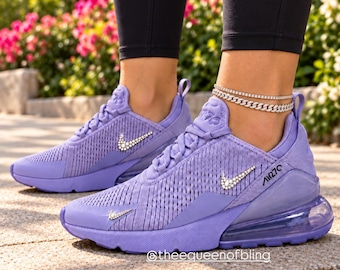May include: Light purple sneakers featuring a mesh upper, a translucent heel air unit, and a rhinestone-encrusted Nike swoosh logo on the side. The text @theequeenofbling is visible near the sole. The shoes have matching purple laces and a structured heel counter.