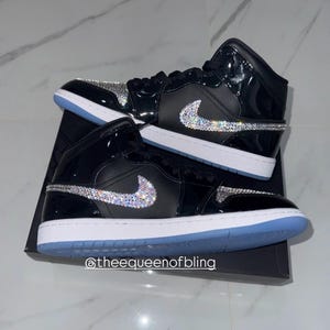 May include: A pair of high-top sneakers in black patent leather with white midsoles and light blue outsoles. The side swoosh logos and toe boxes are embellished with clear, reflective crystals. The text @theequeenofbling is visible.