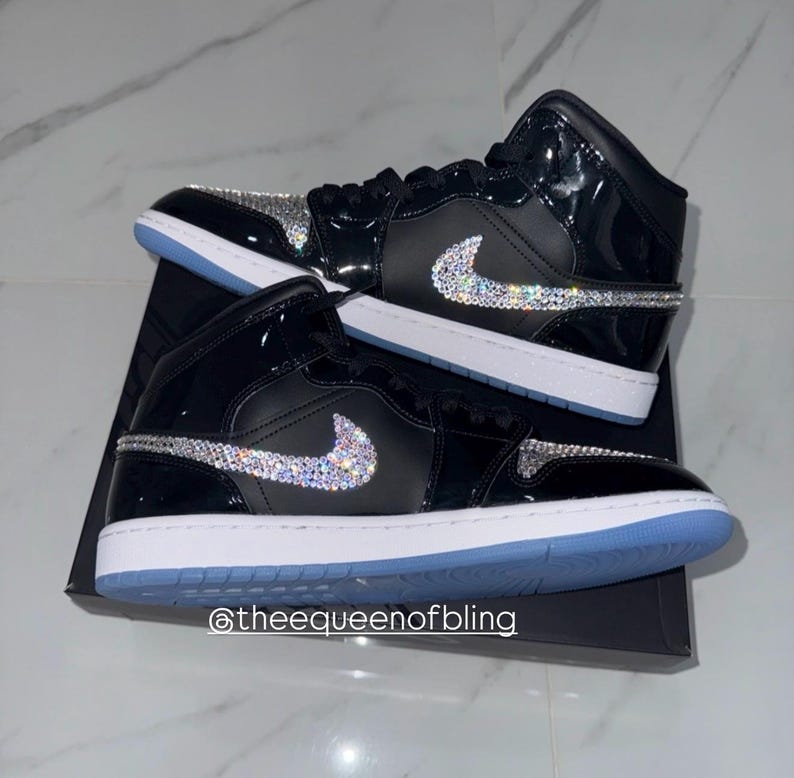 May include: A pair of high-top sneakers in black patent leather with white midsoles and light blue outsoles. The side swoosh logos and toe boxes are embellished with clear, reflective crystals. The text @theequeenofbling is visible.