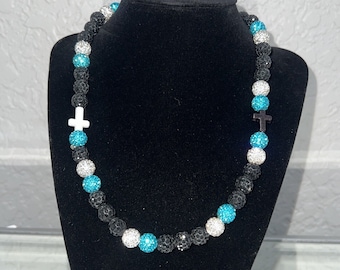 May include: A black beaded necklace with turquoise and white accents. The necklace features two small cross charms.