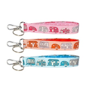 May include: Three colorful keychains with silver key rings. Each keychain features a repeating pattern of vintage camper vans with floral accents. The keychains are pink, orange, and blue.