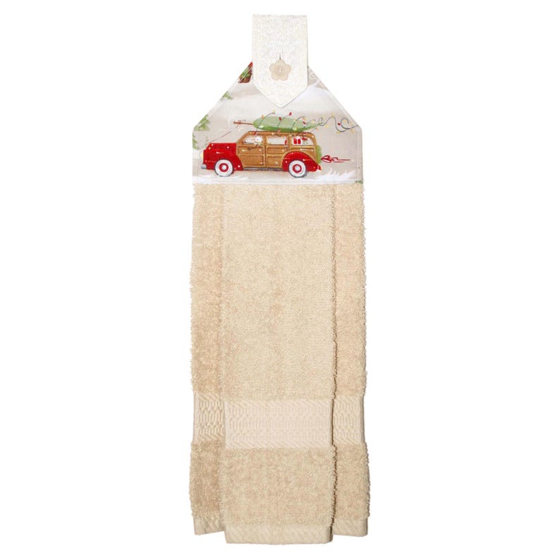 Puede incluir: Un pa&ntilde;o de cocina beige con una parte superior decorativa con un coche familiar bordado en rojo y madera que transporta un &aacute;rbol de Navidad. La toalla tiene un lazo para colgar.