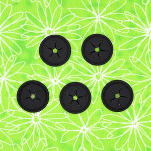 Peut inclure: Cinq organisateurs de câbles en plastique noir avec un motif en forme d'étoile. Les organisateurs sont sur un fond de tissu floral vert et blanc.