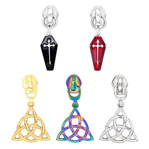 May include: Five metal zipper pulls featuring two coffin-shaped charms in black and red with white cross cutouts, and three triquetra knot charms in gold, iridescent rainbow, and silver finishes, each attached to a standard silver zipper slider.