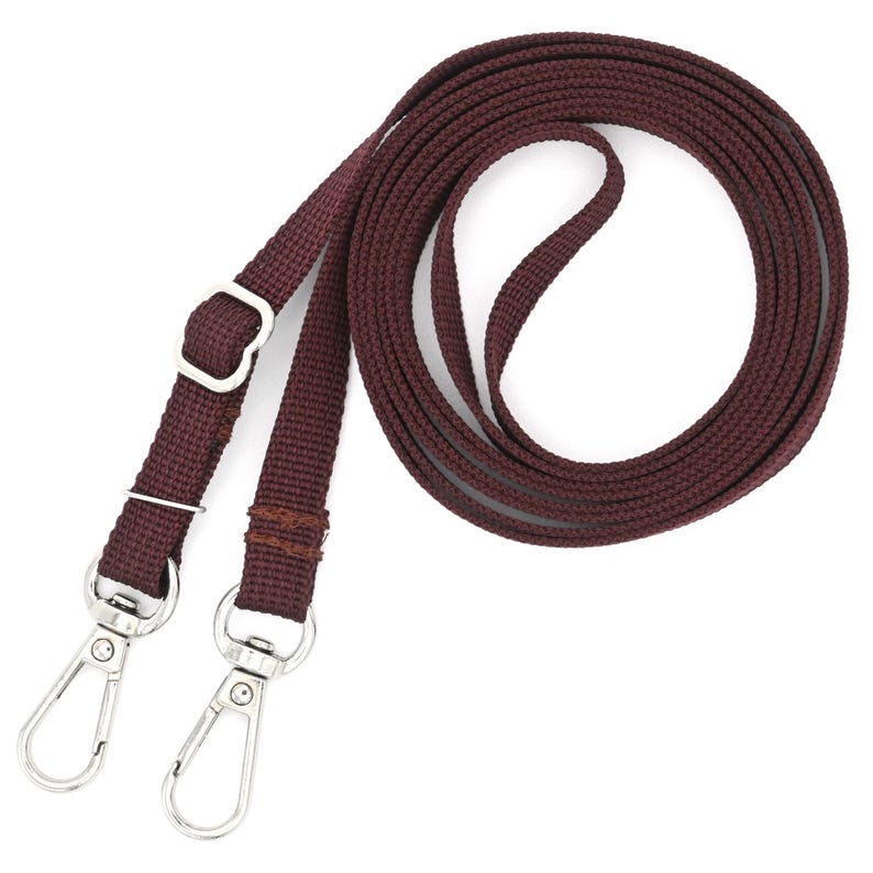 K&ouml;nnte beinhalten: Ein braunes gewebtes Band mit zwei silbernen Drehverschl&uuml;ssen. Das Band ist aufgerollt und bereit, an einer Tasche oder Handtasche befestigt zu werden.