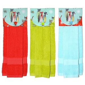 Könnte beinhalten: Drei Küchentücher mit einem Katzendesign auf der oberen Klappe. Die Handtücher sind rot, grün und blau.