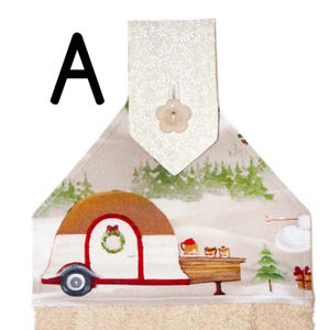 Puede incluir: Un pa&ntilde;o de cocina decorativo con una escena de acampada invernal. El pa&ntilde;o presenta una caravana marr&oacute;n y blanca con ribete rojo, una corona navide&ntilde;a y un paisaje nevado. La parte superior tiene una solapa con estampado floral con un bot&oacute;n en forma de flor.
