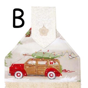 Puede incluir: Toalla colgante con tem&aacute;tica navide&ntilde;a que presenta un coche familiar rojo y marr&oacute;n que transporta un &aacute;rbol de Navidad verde. La toalla tiene un fondo crema con una escena invernal y un bot&oacute;n floral decorativo.