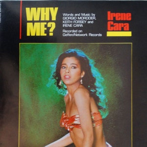 May include: A record cover featuring a woman wearing a red and yellow bikini top and a colorful sarong. The cover is for the song "Why Me?" by Irene Cara. The text "Words and Music by Giorgio Moroder, Keith Forsey and Irene Cara" is printed on the cover.