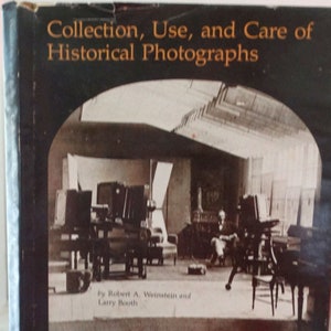 Puede incluir: Portada de libro con fondo negro y texto dorado que dice "Colección, Uso y Cuidado de Fotografías Históricas" por Robert A. Weinstein y Larry Booth. La imagen de la portada muestra un estudio de fotografía vintage con un fotógrafo sentado en una silla.