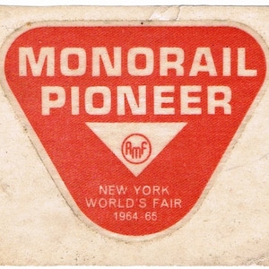 May include: Red triangular sticker with white text that reads "MONORAIL PIONEER" and a smaller white triangle with the letters "AMF" inside. Below the triangle is the text "NEW YORK WORLD'S FAIR 1964 65".