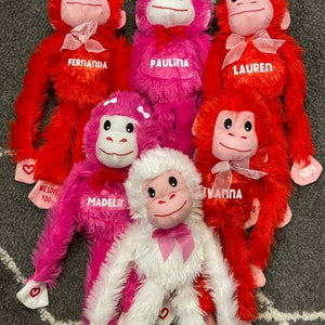 May include: Six plush monkey toys with pink and red fur. The monkeys have pink bows and are personalized with names: Fernanda, Paulina, Lauren, Madeline, and Yvanna. The monkeys have a heart-shaped tag that says "We love you".
