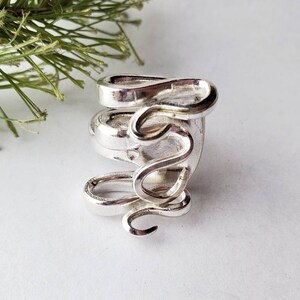 May include: A silver ring with a unique, abstract design. The ring is made of twisted metal and has a smooth, polished finish.
