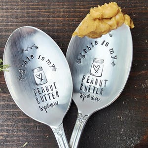May include: Two silver spoons with the text "This is my peanut butter spoon" engraved on them. One spoon has peanut butter on it.