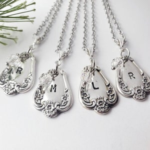 May include: Three silver necklaces with personalized initial charms. Each charm is a vintage spoon with a floral design and a single initial engraved on it. The initials are R, M, and L.