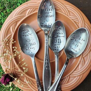 May include: Four vintage silver spoons with stamped text and pumpkin designs. The spoons are arranged on a terracotta plate. Text includes "falling for cozy nights", "give em to talk about", "bet the leaves fall where they may", and "pumpkin spice makes mama nice".