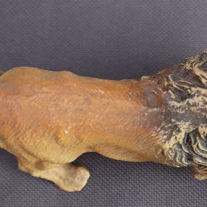 K&ouml;nnte beinhalten: Detaillierte Figur eines L&ouml;wen in Laufpose. Der L&ouml;we ist haupts&auml;chlich hellbraun mit einer dunkelbraunen M&auml;hne. Die Skulptur besteht aus einem festen Material und ist vor einem dunkelgrauen Hintergrund platziert. Der Schwanz des L&ouml;wen ist ausgestreckt.