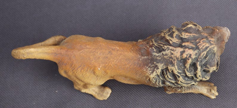 K&ouml;nnte beinhalten: Detaillierte Figur eines L&ouml;wen in Laufpose. Der L&ouml;we ist haupts&auml;chlich hellbraun mit einer dunkelbraunen M&auml;hne. Die Skulptur besteht aus einem festen Material und ist vor einem dunkelgrauen Hintergrund platziert. Der Schwanz des L&ouml;wen ist ausgestreckt.