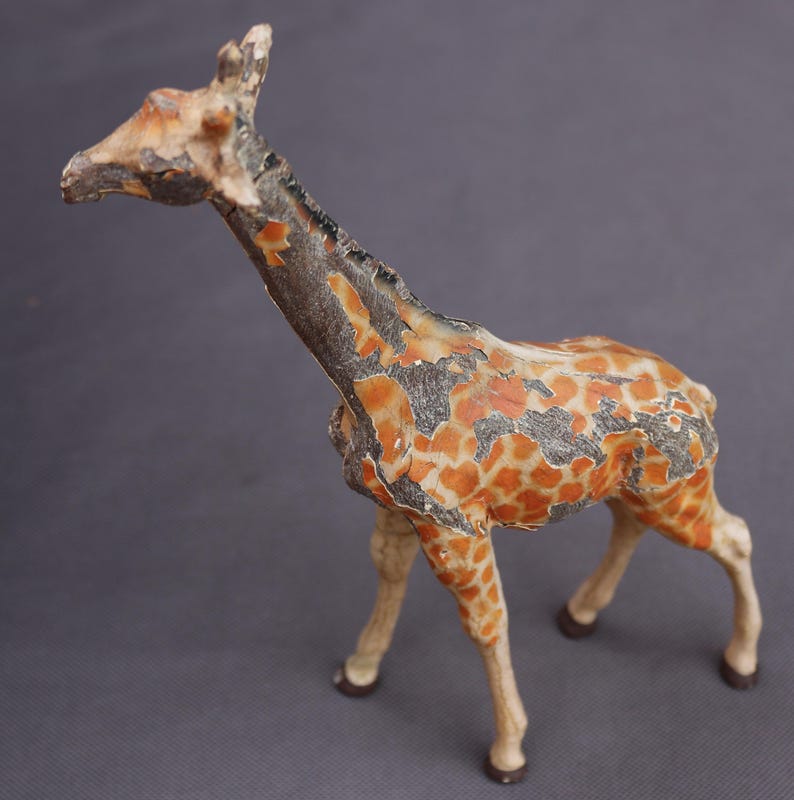 K&ouml;nnte beinhalten: Vintage Giraffenfigur mit einem Used-Look. Die Giraffe hat einen beigefarbenen K&ouml;rper mit orangefarbenen und braunen Flecken, einen langen Hals und vier Beine. Die Figur besteht aus einem harten Material und hat ein verwittertes Aussehen.
