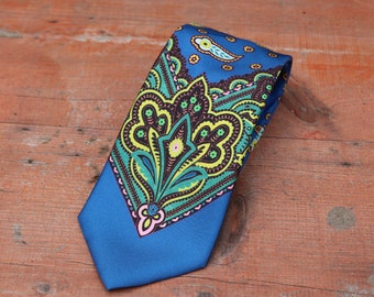Pode incluir: Uma gravata azul com padrão paisley com detalhes em verde, amarelo, rosa e preto.