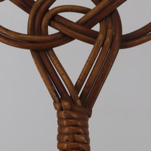 Pu&ograve; includere: Primo piano di uno schienale di sedia in vimini intrecciato, che mostra il nodo intricato del rattan marrone.