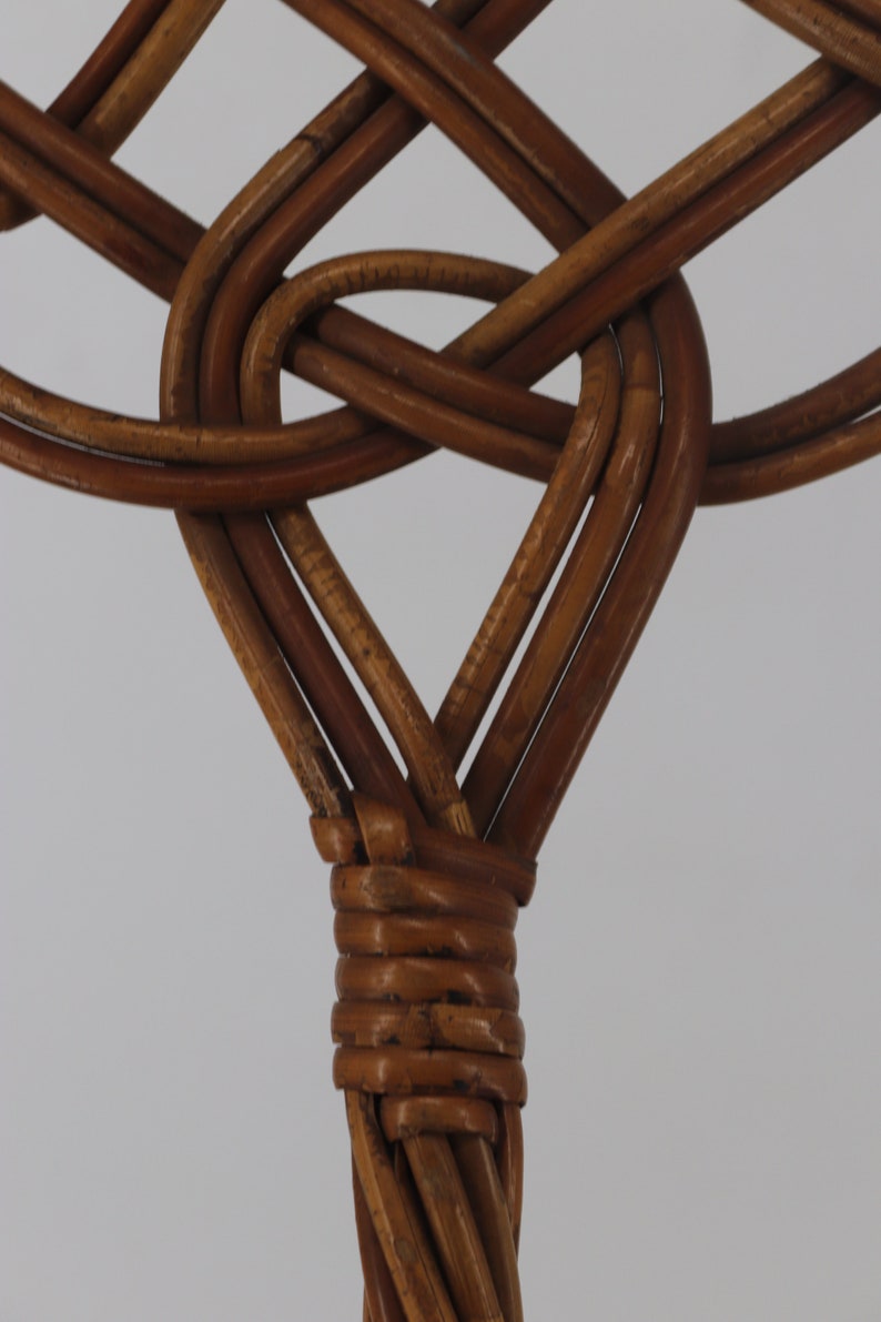 Pu&ograve; includere: Primo piano di uno schienale di sedia in vimini intrecciato, che mostra il nodo intricato del rattan marrone.