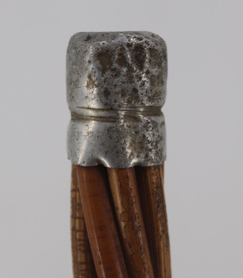 Pu&ograve; includere: Primo piano della parte superiore di un bastone con un tappo in metallo argentato. Il bastone &egrave; fatto di canne marroni intrecciate.