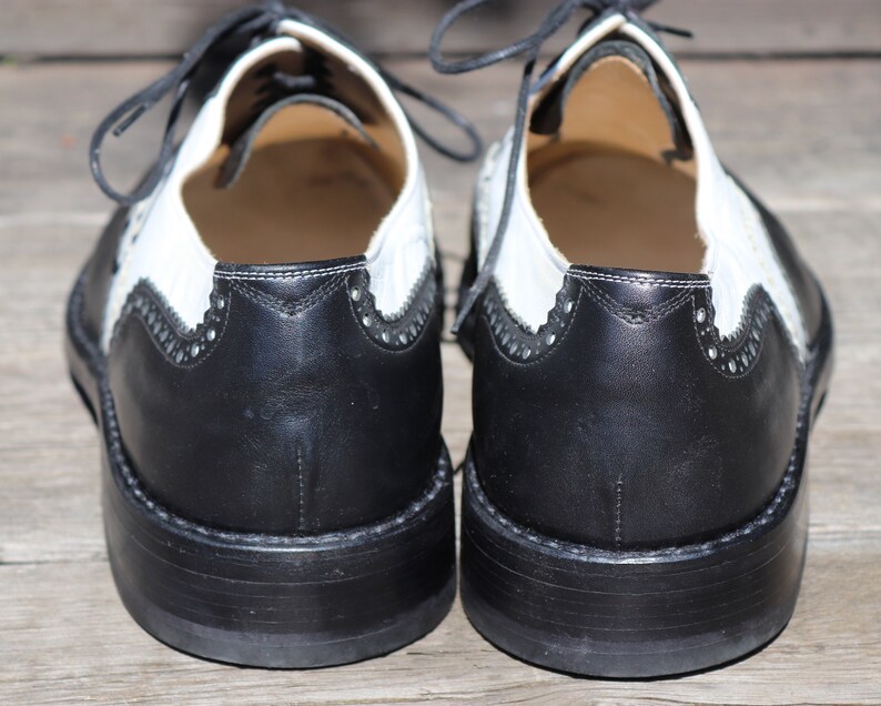Op de afbeelding: Een paar tweekleurige leren Oxford-schoenen. De schoenen hebben een zwarte neus en hiel met een wit bovenwerk. Het ontwerp omvat decoratieve perforaties en zwarte veters. De zolen zijn zwart en hebben een dikke, gestapelde uitstraling.