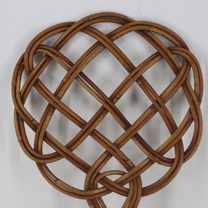 Pu&ograve; includere: Un decoro da parete a forma di cuore in vimini intrecciato marrone con un motivo a croce.