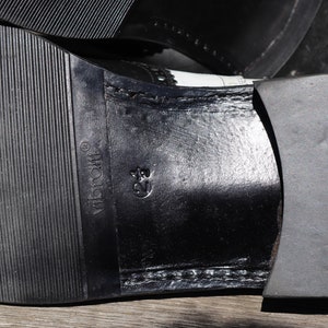 Op de afbeelding: Close-up van de zool van een zwart-witte leren schoen. De rubberen zool heeft een textuurpatroon met de merknaam "Vibram" zichtbaar. De schoenmaat is gemarkeerd als 39.