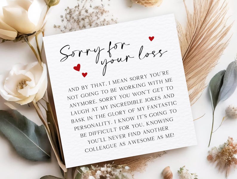 May include: A white card with the text "Sorry for your loss" in black script, with three red heart accents. The card's message continues in a smaller, black sans-serif font. The card is surrounded by white flowers and dried foliage.