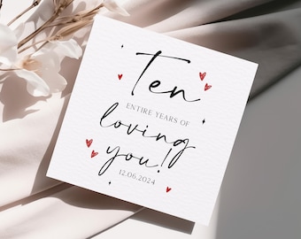 May include: A white card with black text that reads "Ten Entire Years of Loving You!" with the date "12.06.2024" below. The card is decorated with small red hearts.