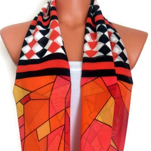 Könnte beinhalten: Ein farbenfroher Infinity-Schal mit einem geometrischen Muster in Orange-, Rot- und Gelbtönen. Der Schal hat an den Enden ein schwarz-weißes Karomuster.