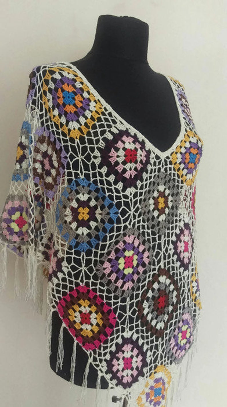 May include: A white crochet top with a colourful geometric pattern. The top has a V-neck and fringe trim.