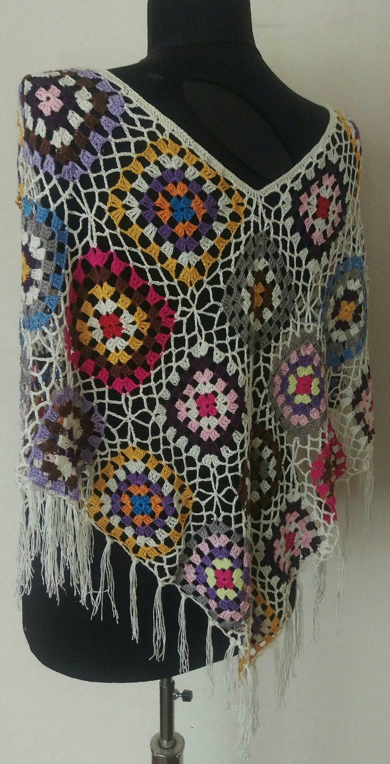 May include: A crocheted poncho featuring a colourful granny square pattern and white fringe. The poncho is made in a range of colours, including pink, purple, blue, green, yellow and orange.