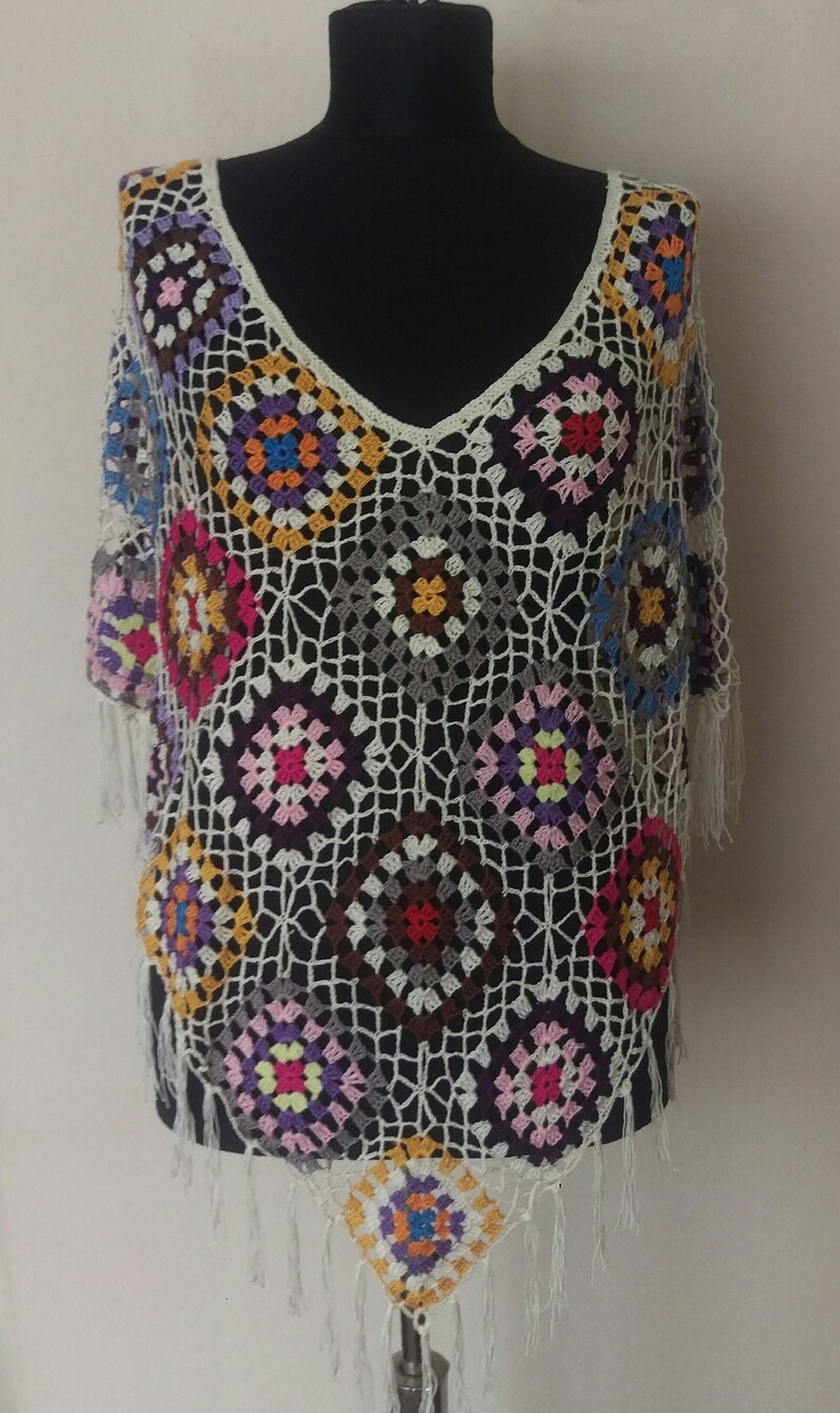 May include: A white crochet top with a colourful geometric pattern. The top has a V-neck and fringe trim.