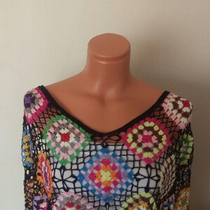 May include: A black crochet top with a colourful geometric pattern. The top has a V-neck and is made of a lightweight, airy fabric.