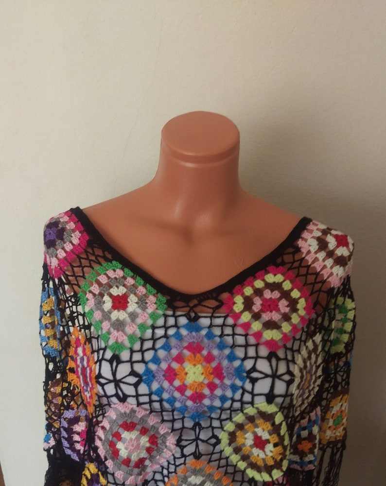 May include: A black crochet top with a colourful geometric pattern. The top has a V-neck and is made of a lightweight, airy fabric.
